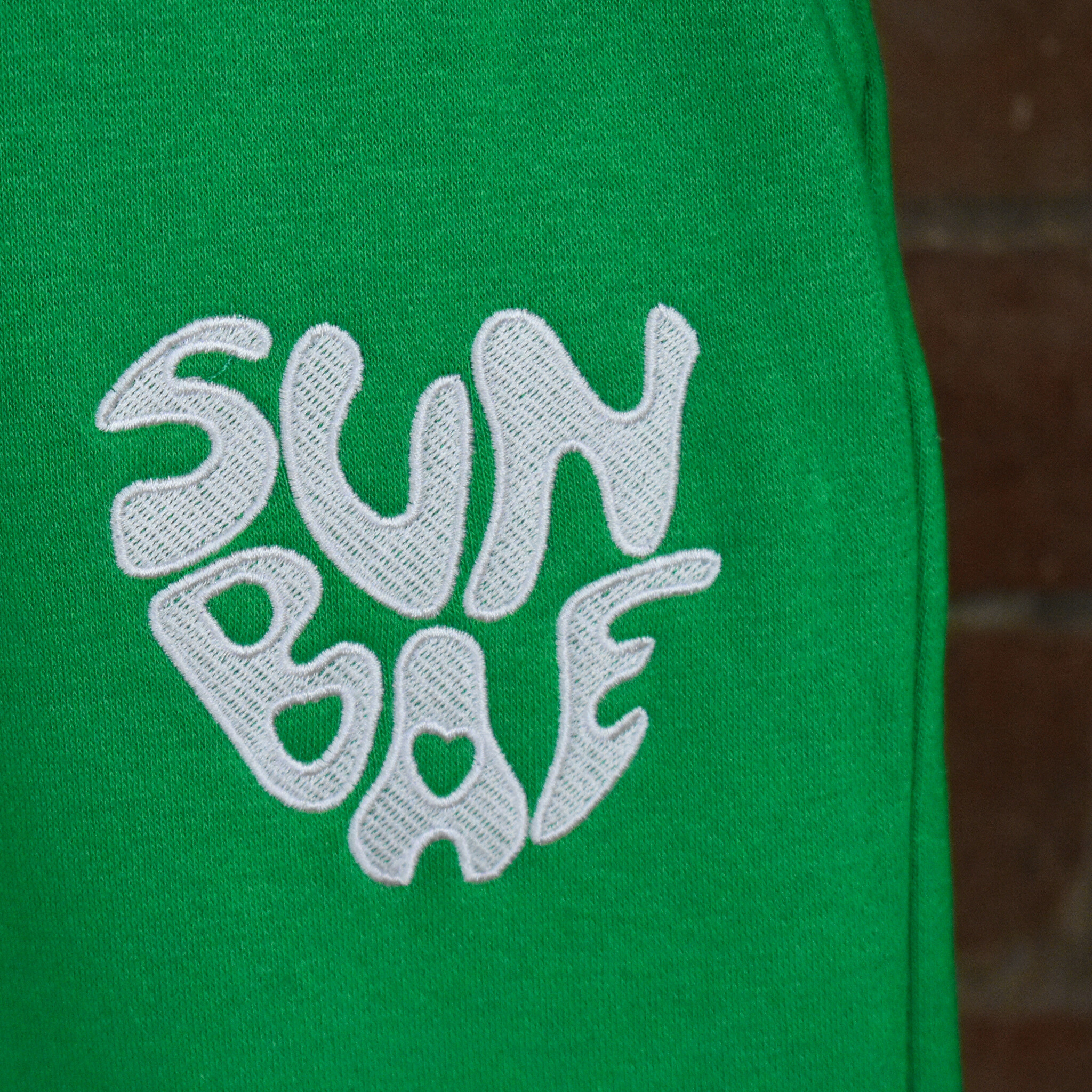 Green Sweat Pant with SUNBAE logo embroidered in white on a brick background