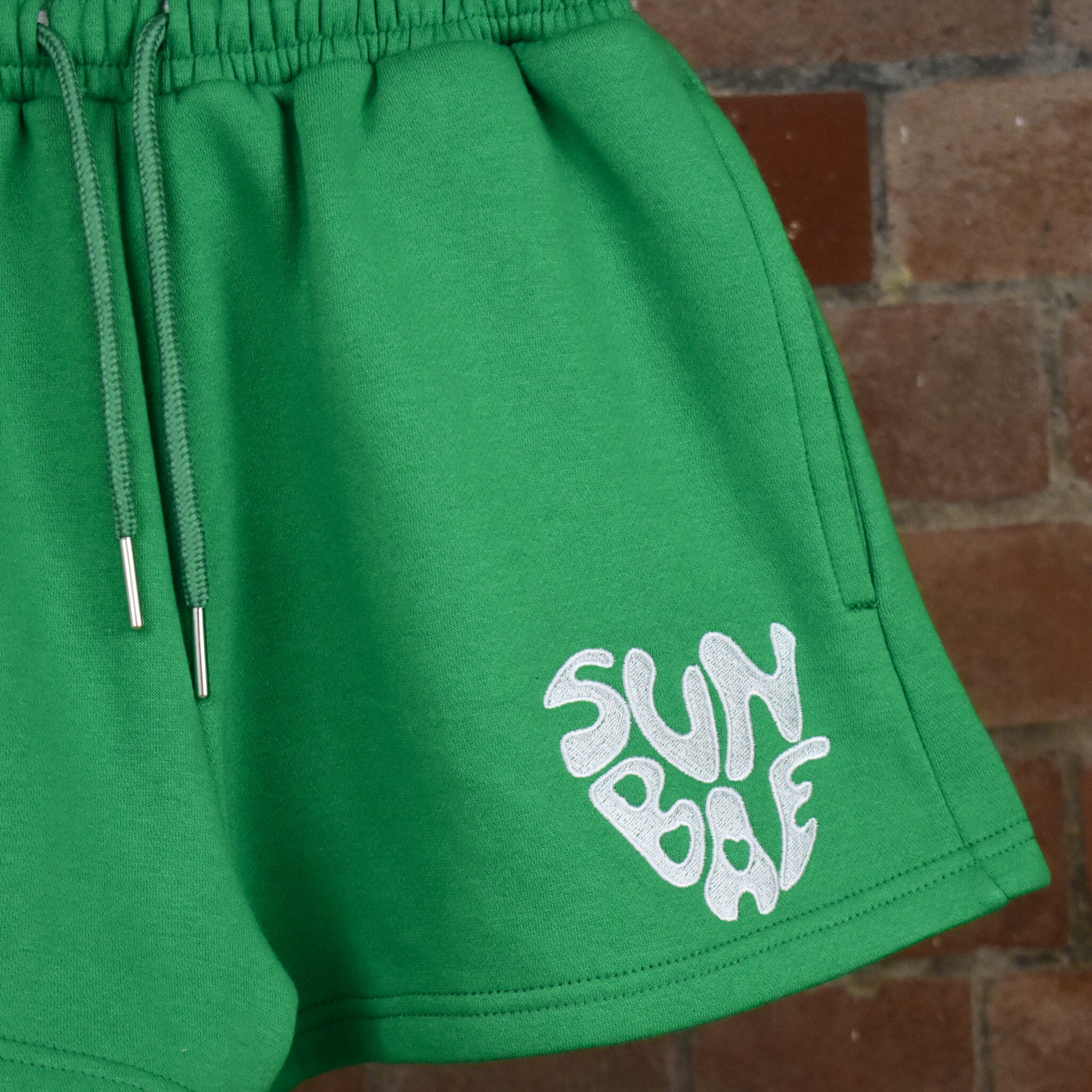 Green Shorts with SUNBAE logo embroidered in white on a brick background