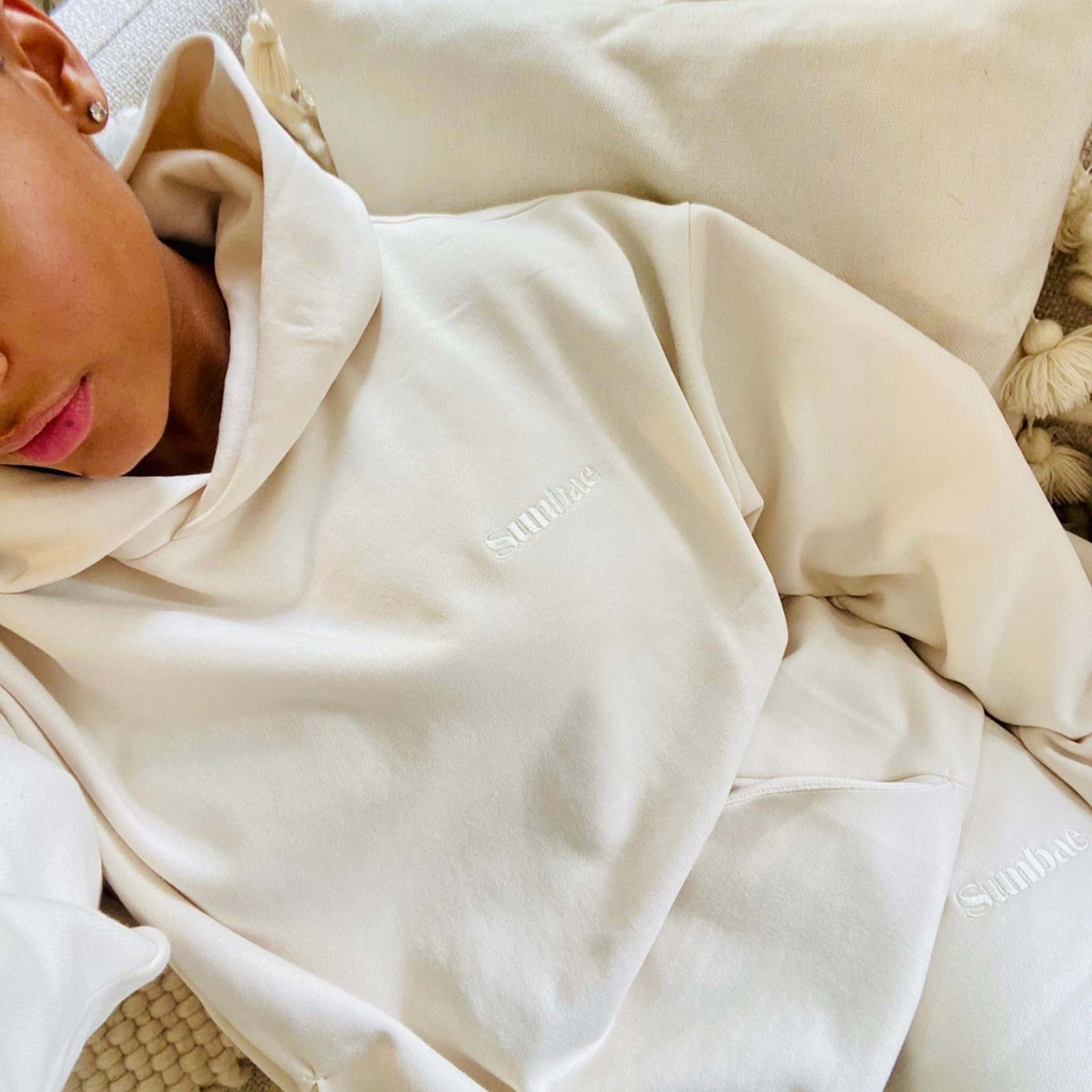 Person wearing Sunbae Hoodie and Shorts, lying on a bed.