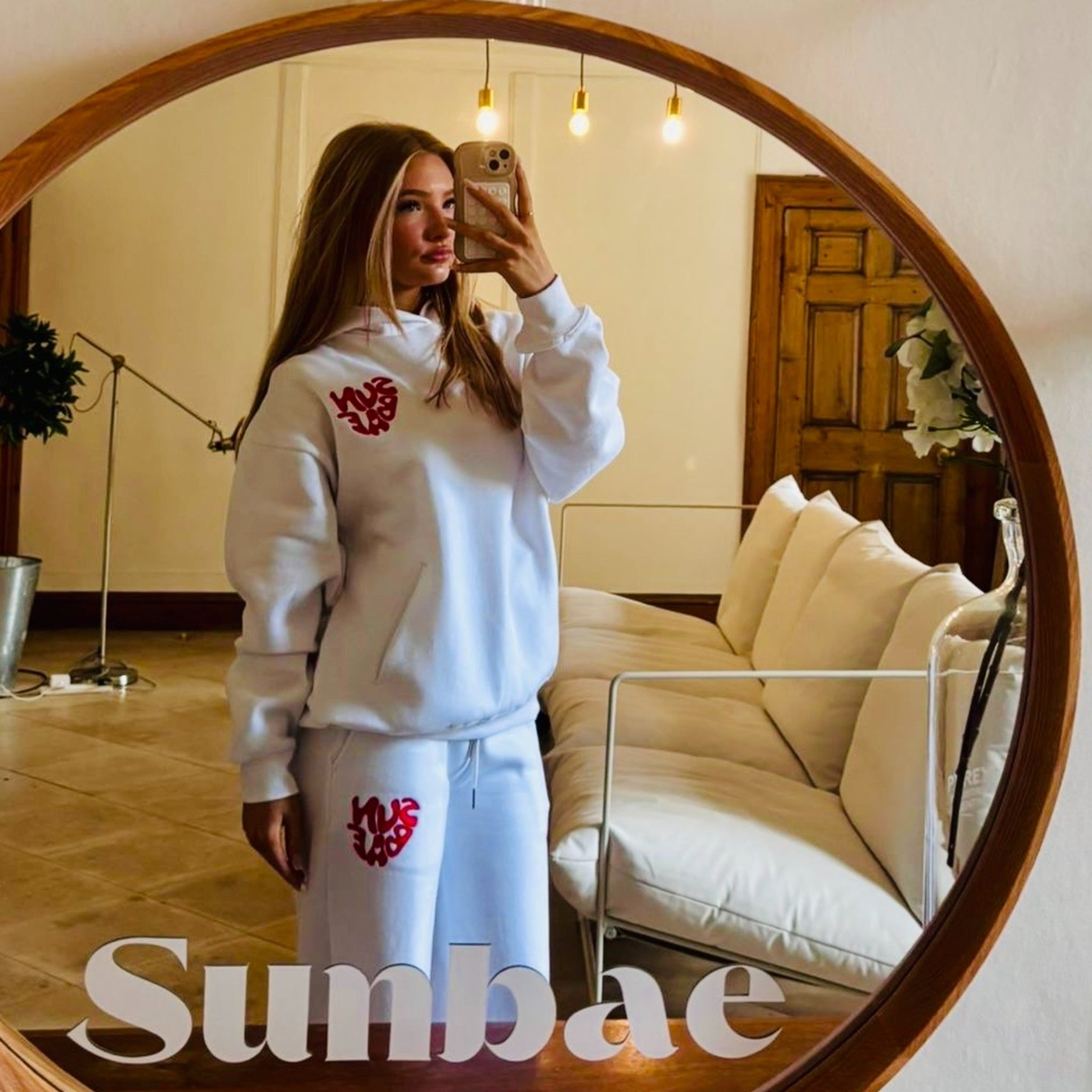 Person wearing a white outfit with red logo in front of a round mirror, with 'Sunbae' branding.