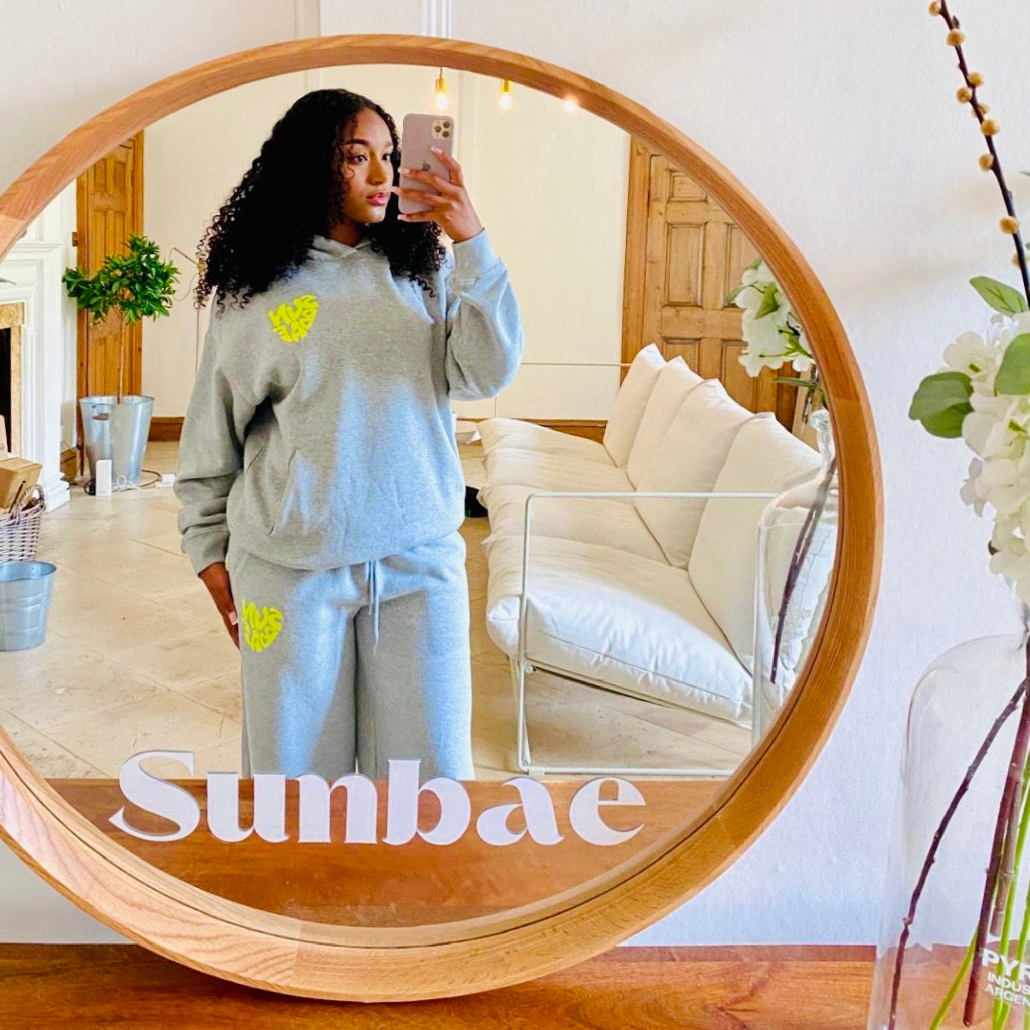 Person taking a mirror selfie wearing a gray SUNBAE outfit in a living room.