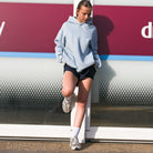 Yvonne Main wearing a light blue Sunbae hoodie and black shorts standing in front of a red and white wall.