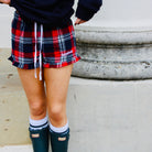 Person wearing plaid shorts and green rain boots on a stone surface.