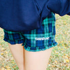 Person wearing plaid shorts with 'Sunbae' branding and rain boots on a grassy ground.