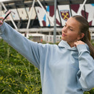 Yvonne Main wearing a Sunbae hoodie taking a selfie in front of a stadium with branding in the background