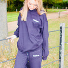 Person wearing a purple tracksuit with visible branding in an outdoor setting.
