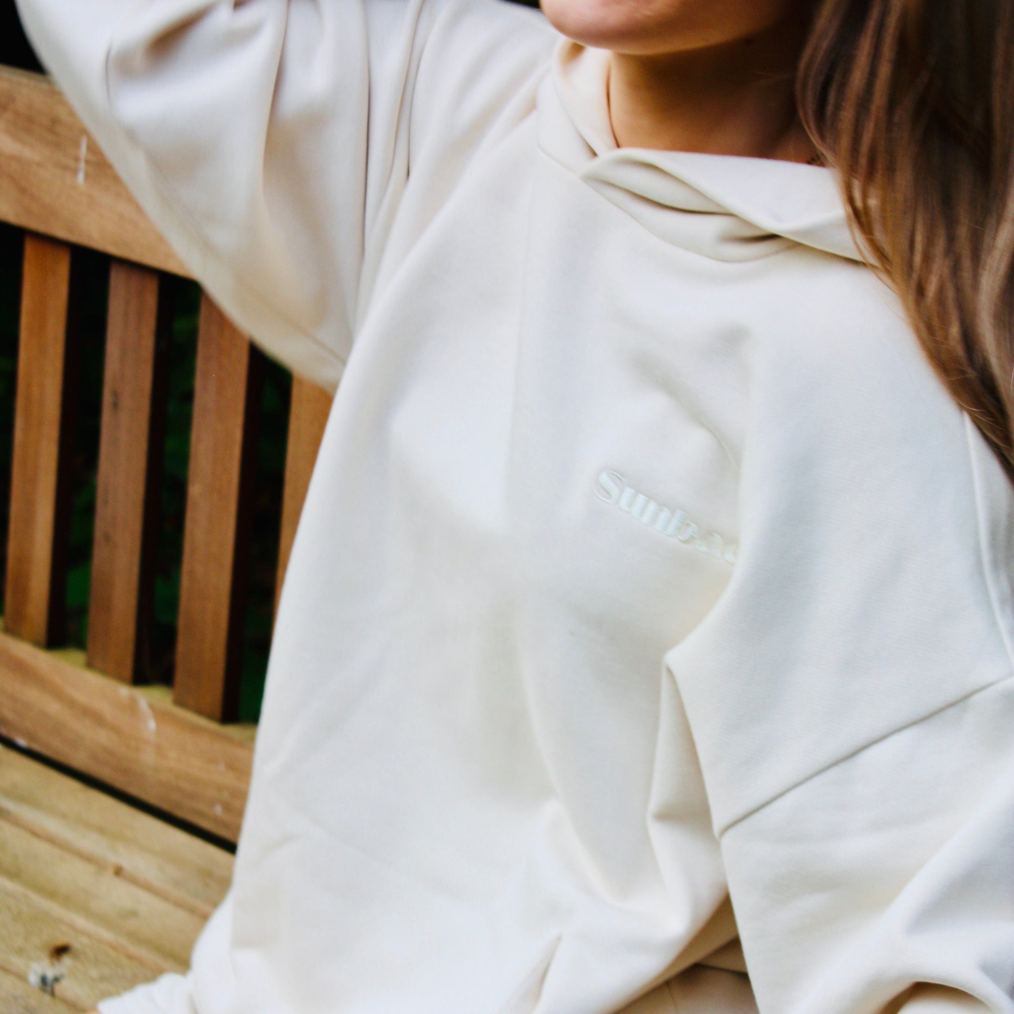 Person wearing a white hoodie and shorts sitting on a wooden bench.