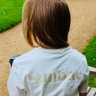 Person wearing a white t-shirt with 'Sunbae Glow' text, sitting on a wooden bench outdoors.