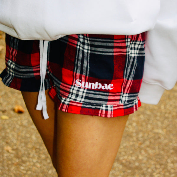 Plaid shorts with 'Sunbae' logo worn by a person, blurred background