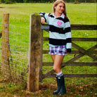 Person standing by a wooden gate in a grassy field with trees in the background