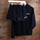 Navy hoodie and shorts set with 'Sunbae' branding on a rack against a brick wall.