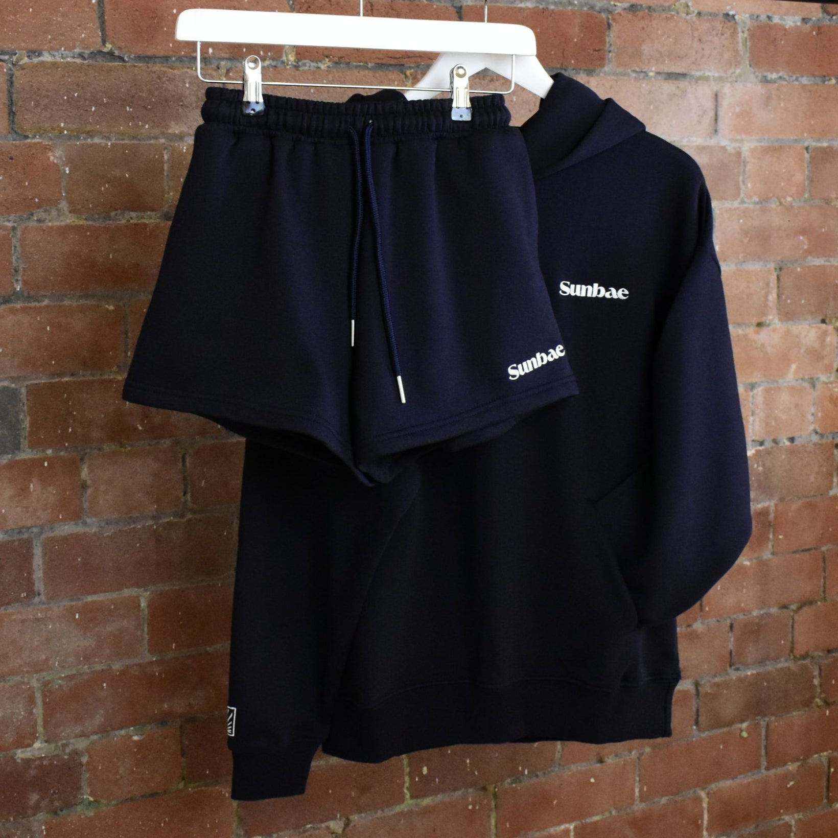Navy hoodie and shorts set with 'Sunbae' branding on a rack against a brick wall.