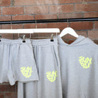 Grey SUNBAE Sweat Pants and Hoodie on hangers against a brick wall.