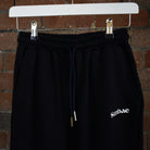 Navy SUNBAE Sweat Pants with branding on a hanger against a brick wall.
