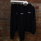Navy SUNBAE hoodie and Jogger with logo on a hanger against a brick wall 