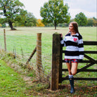 Woman in a rugby jersey standing by a wooden gate in a field