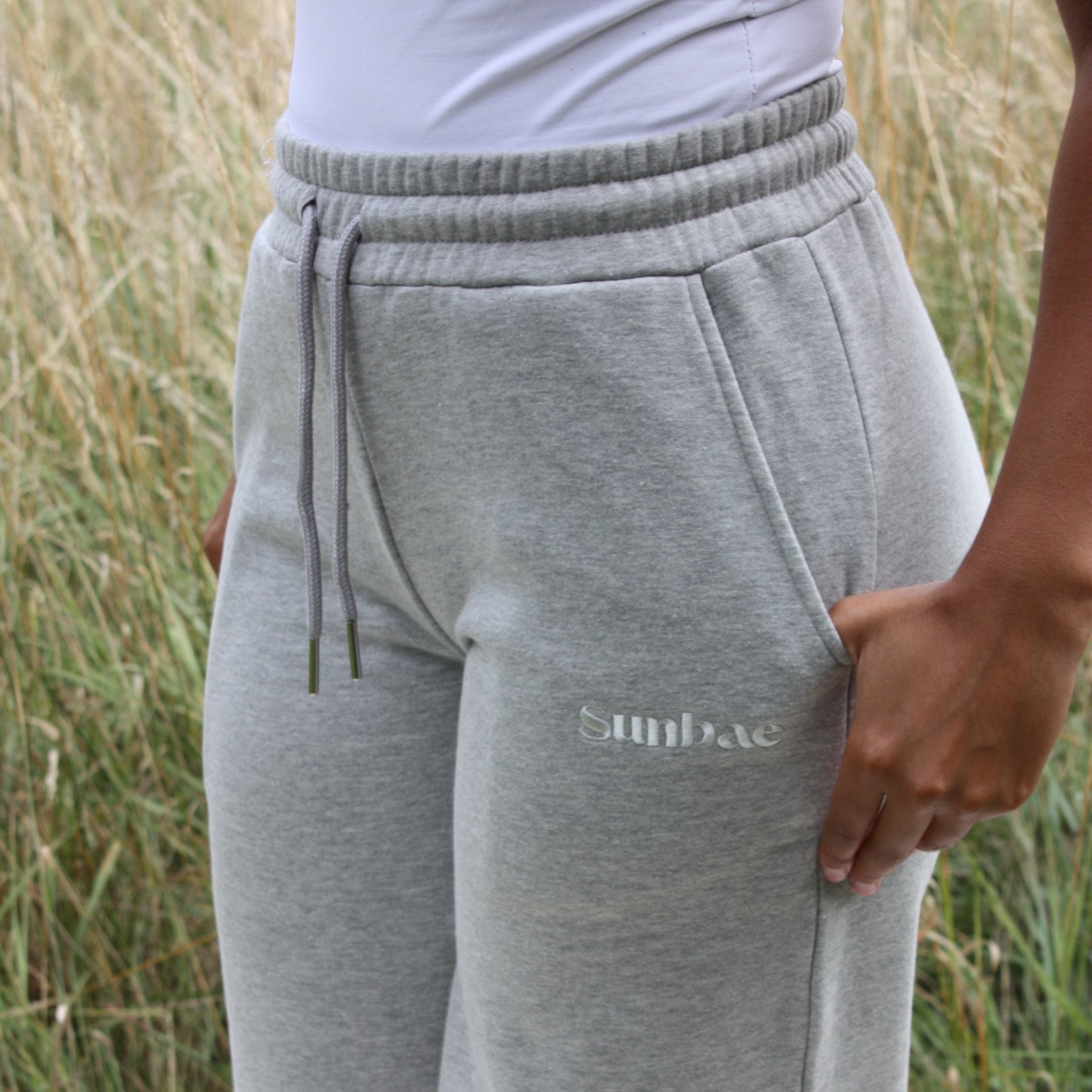 Grey Sunabe sweatpants with a brand logo worn by a person in a grassy outdoor setting