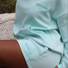 Person wearing a mint Sunbae hoodie and shorts sitting outdoors.