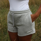 Person wearing a white tank top and gray Sunbae shorts in a grassy field