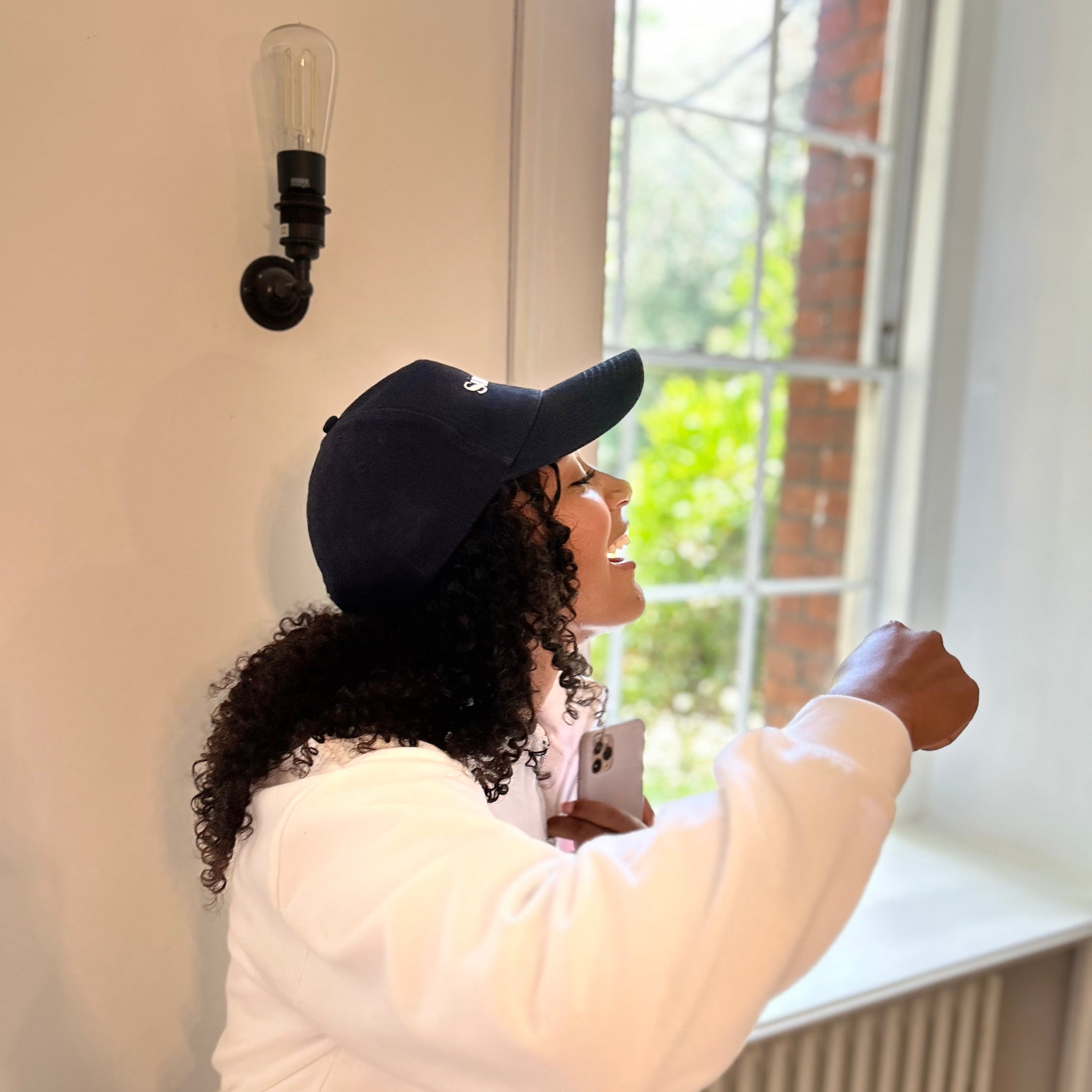 Person wearing a navy cap and white coat standing by a window with a light bulb wall fixture.