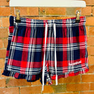 Plaid shorts with SUNBAE logo hanging on a brick wall.