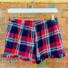 Plaid SUNBAE shorts hanging on a wooden rack against a brick wall.