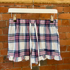 Plaid SUNBAE shorts with ruffles on a hanger against a brick wall