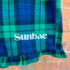 Blue and green plaid fabric with 'Sunbae' text against a brick wall background