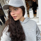 Person wearing a grey SUNBAE sweatshirt and hat indoors with a blurred background