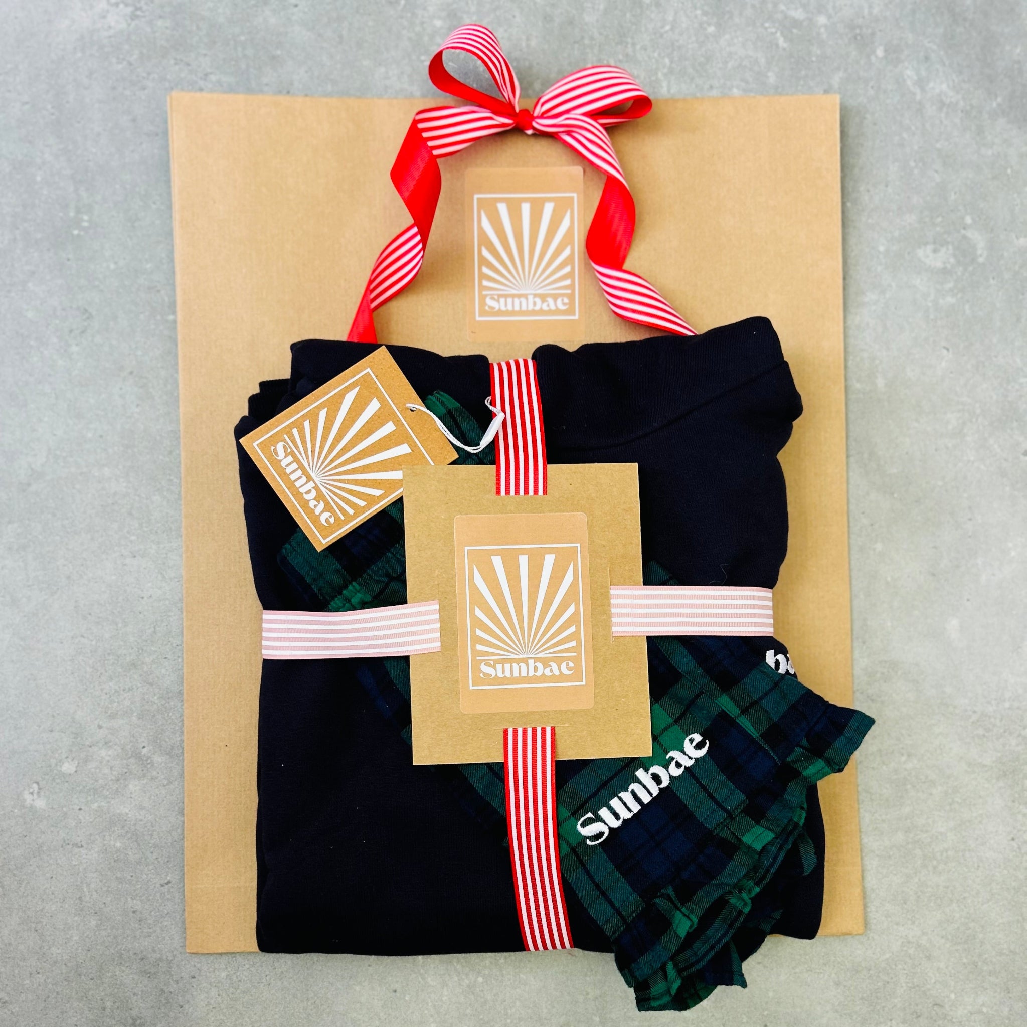 Packaged SUNBAE Shorts and Hoodie with a red ribbon on a gray surface