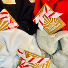 Collection of colourful SUNBAE hair scrunchies with SUNBAE tags on a red and pink background.