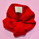 Red SUNBAE scrunchie with a SUNBAE label on a pink surface
