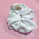White SUNBAE scrunchie with a SUNBAE label on a pink background.