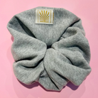 Grey Marl SUNBAE scrunchie with a SUNBAE label on a pink background.