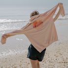 Person on a beach holding a Coral Sunbae Hoodie 