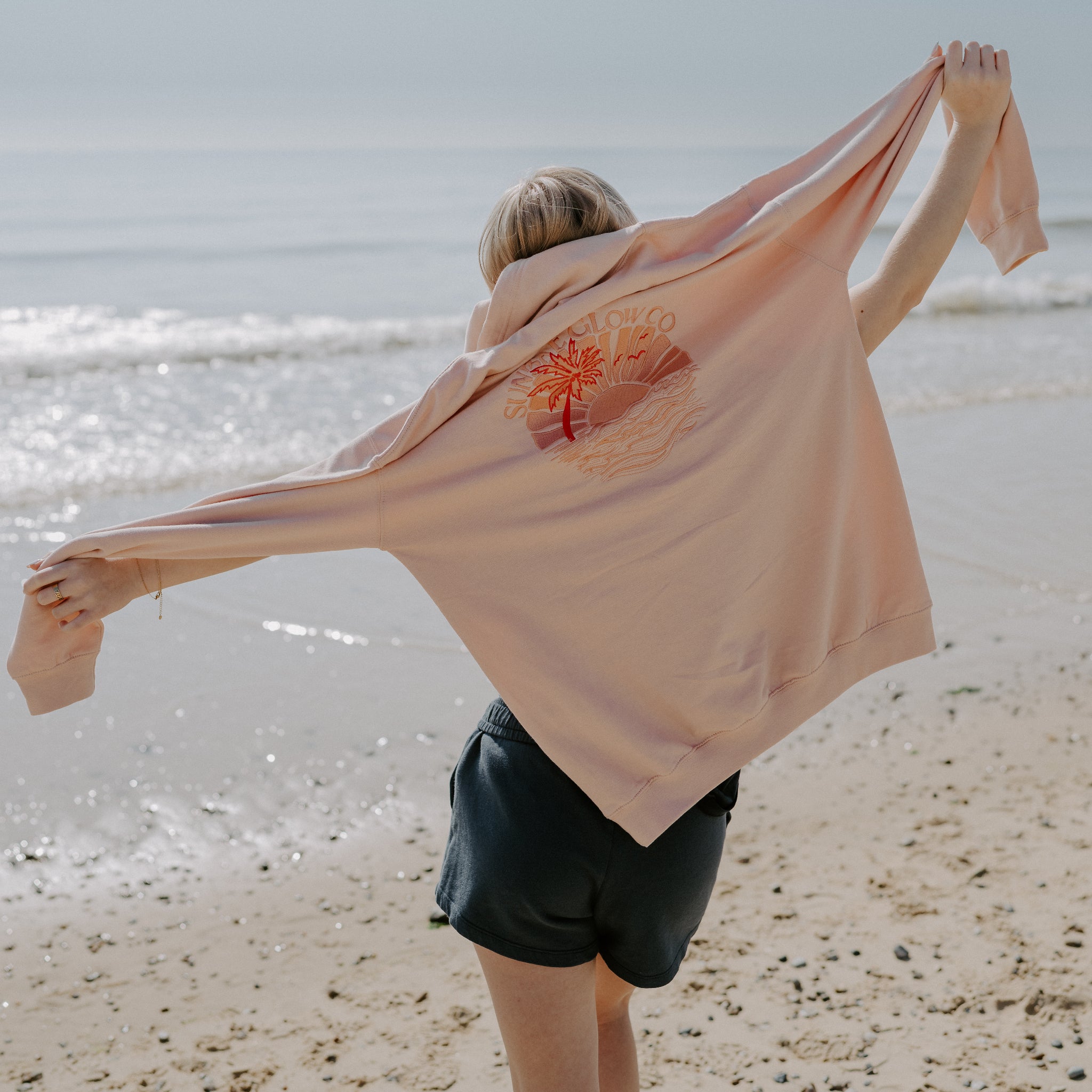 Person on a beach holding a Coral Sunbae Hoodie 
