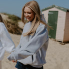A woman standing on a beach wearing the SUNBAE grey marl oversized hoodie on the beach.