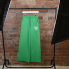 Green SUNBAE Sweat Pants on a hanger against a brick wall