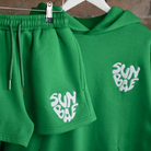 Green Shorts and Hoodie on hangers with SUNBAE logo embroidered in white on a brick background