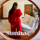 Person wearing a red tracksuit with 'Sunbae' branding in a living room.