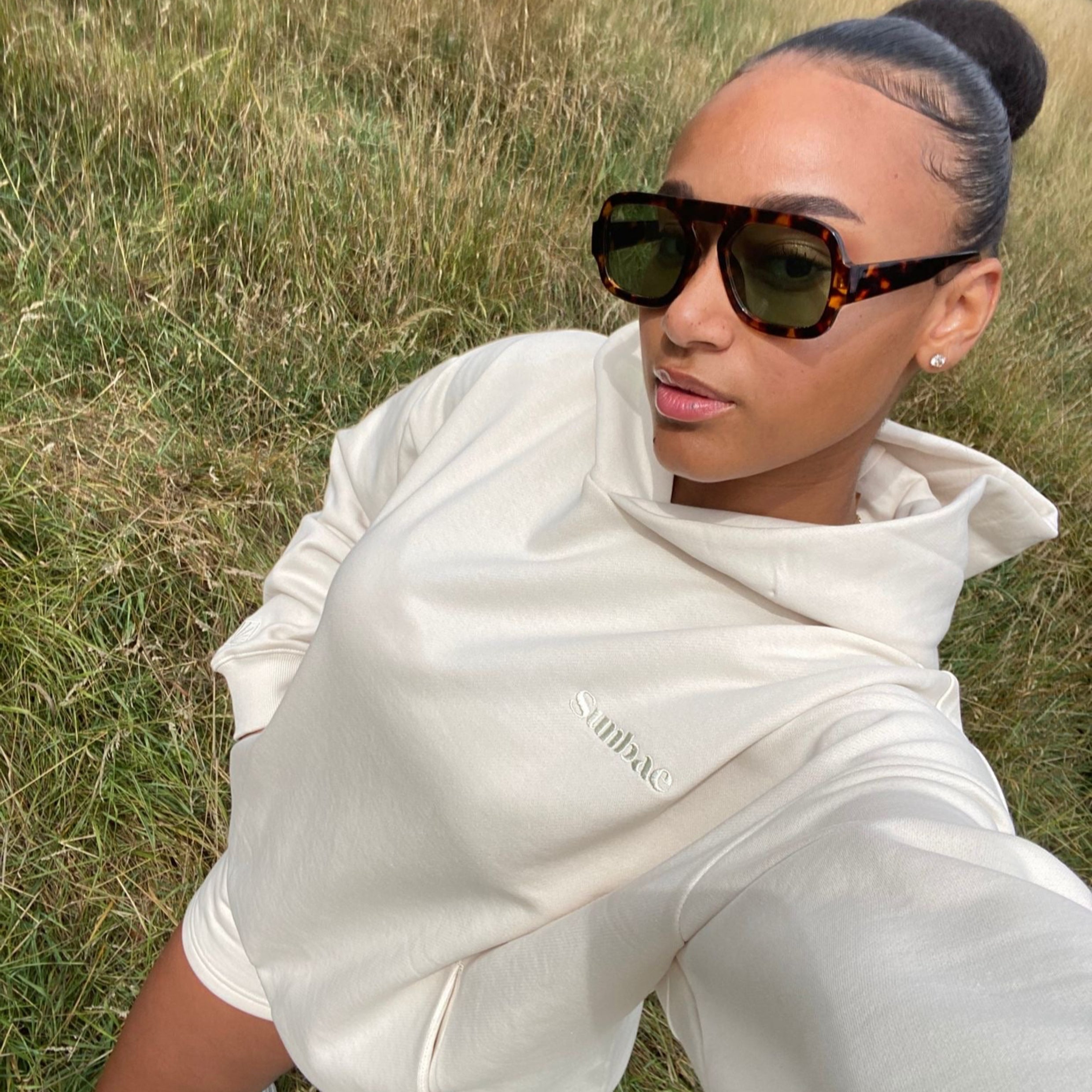 Person wearing a ivory Sunbae hoodie  in a grassy field.